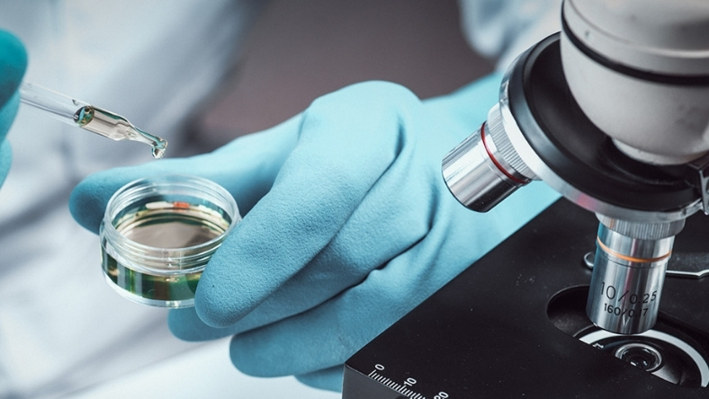 Gloved hand holding lab sample beside microscope equipment